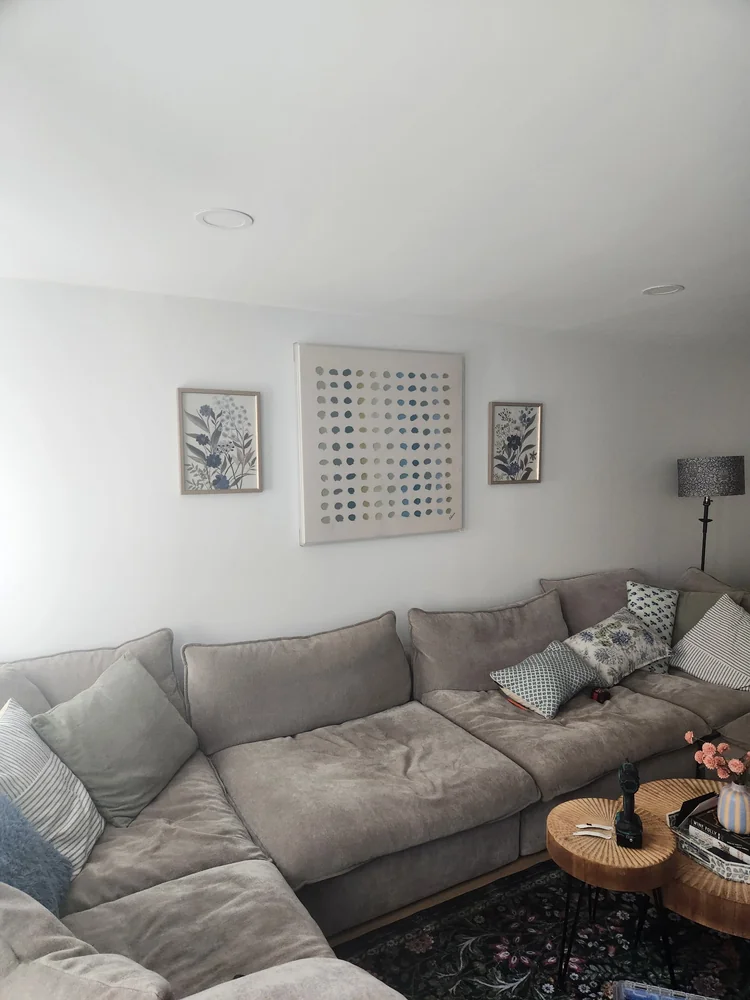 Three framed artworks arranged above a gray living room sofa